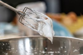 metal beater with whipped cream on it over a metal mixing bowl