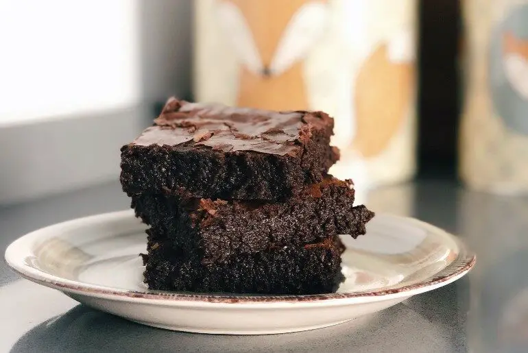 3 brownies stacked on a white plate in front of ceramic jars