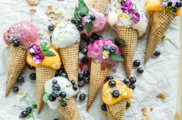 pink, orange, and white ice creams in waffle cones sprinkled with flowers and blueberries