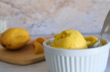 vibrant yellow ice cream in a white ramekin with a half cut up mango in the background