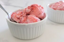 3 scoops of strawberry ice cream in a white bowl with a spoon