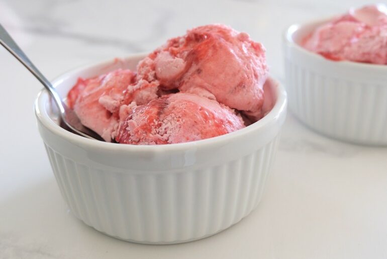 3 scoops of strawberry ice cream in a white bowl with a spoon