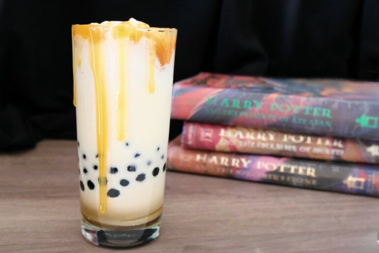 tall glass containing a milkshake and boba with a black background