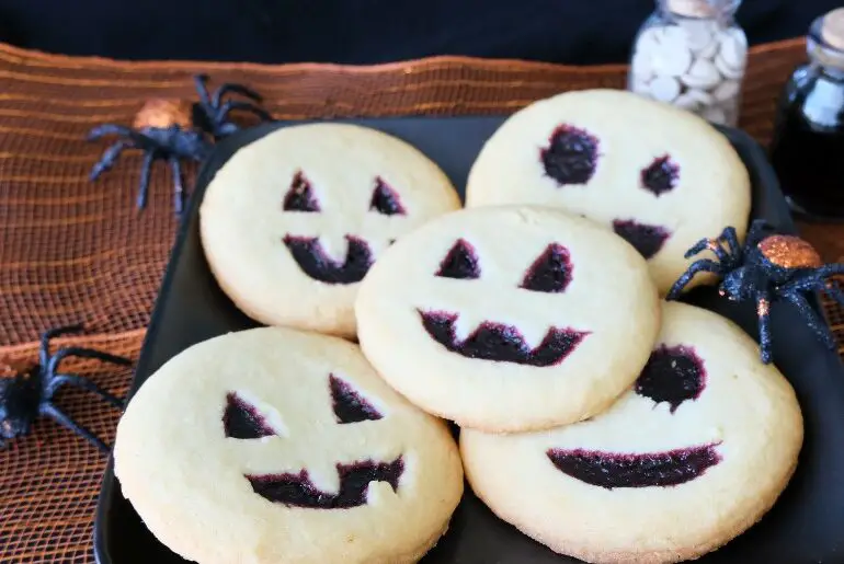 5 jack-o-lantern cookies on a black plate with an orange background