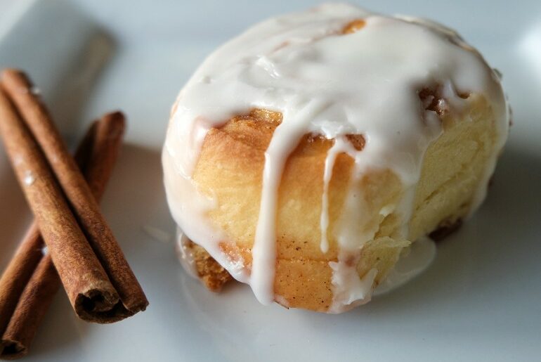 one cinnamon roll on a white plate with cinnamon sticks