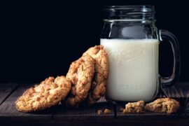 a glass mug of milk with cookies leaned on it with a black background