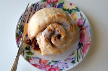 cinnamon roll drizzled with glaze on a floral plate. A fork rests on the plate and the cinnamon roll has a bite taken out.